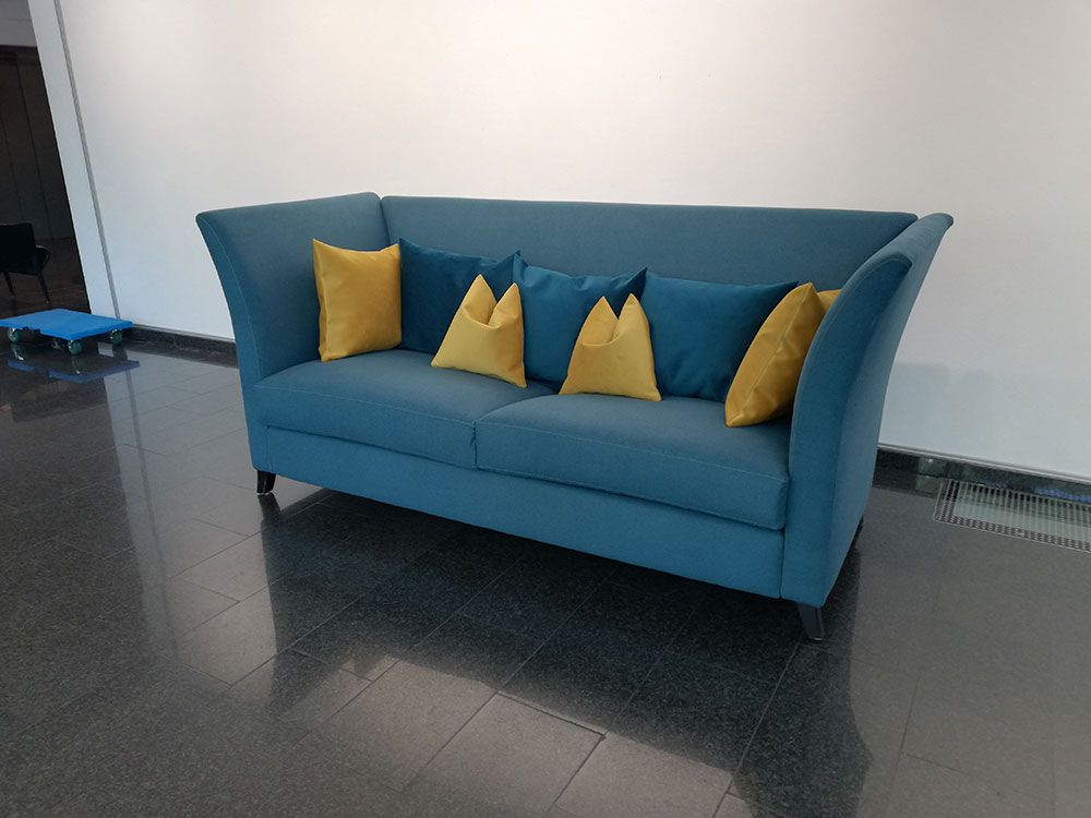 Auf einem gefliesten Boden steht ein blaues Sofa mit gelben Kissen.