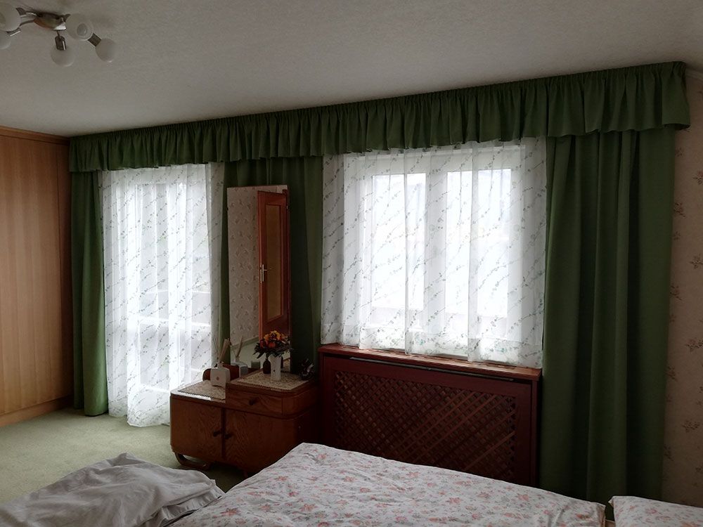 Ein Schlafzimmer mit zwei Betten, einer Kommode, einem Spiegel und grünen Vorhängen.