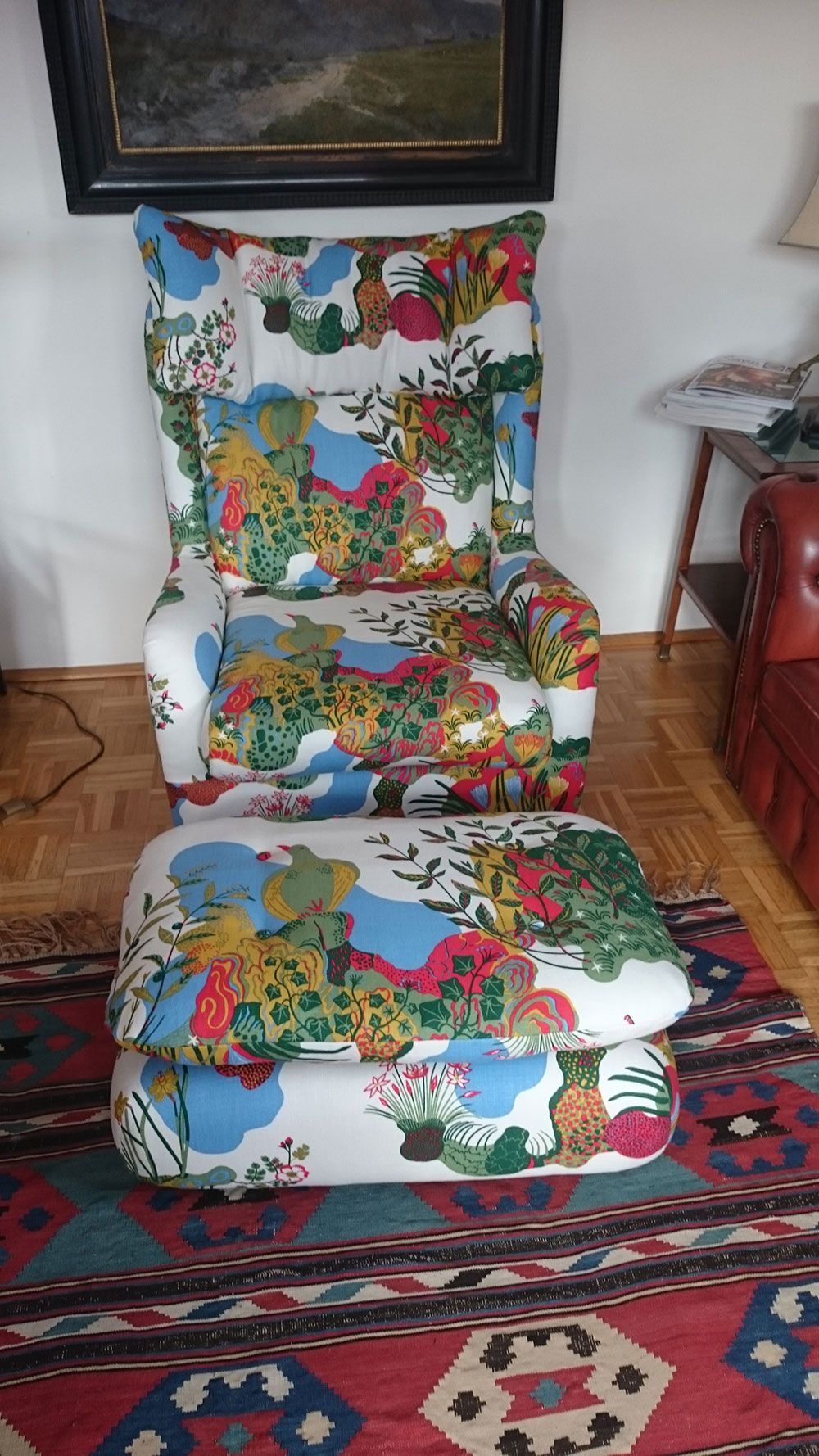 Ein bunter Sessel und ein Ottomane stehen auf einem Teppich in einem Wohnzimmer.