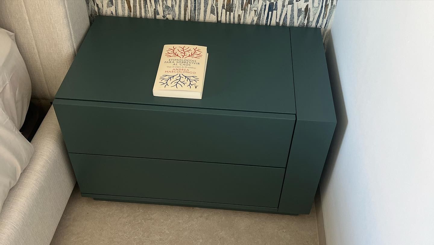 Una mesita de noche verde en un dormitorio junto a una cama.