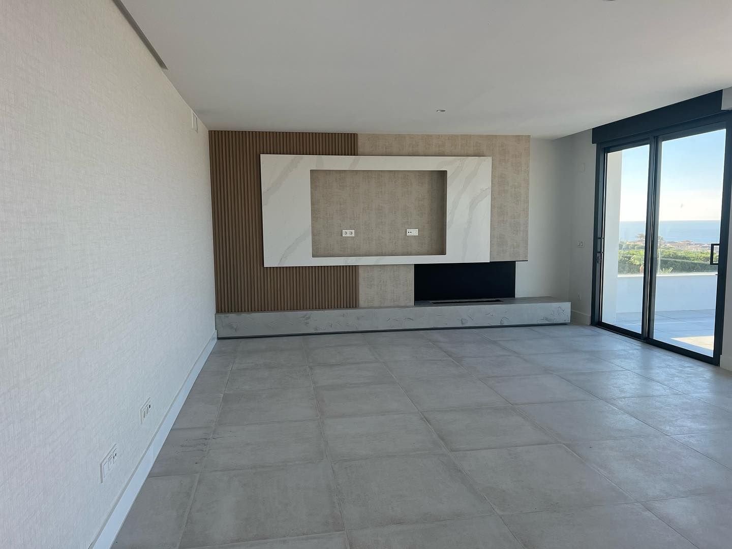 Una sala de estar vacía con un televisor en la pared y puertas corredizas de vidrio.