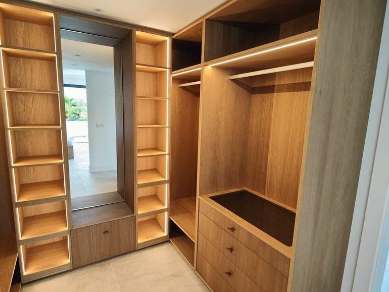 Un vestidor con estantes y cajones de madera y un espejo.