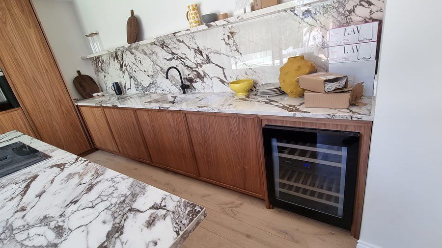 Una cocina con encimeras de mármol y gabinetes de madera y un enfriador de vinos.