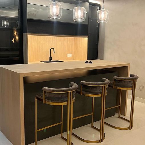 Una cocina con una encimera larga y tres taburetes de bar.