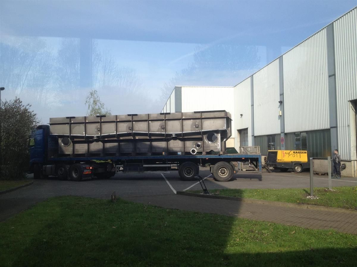 Ein LKW transportiert ein großes Stück Metall vor einem Gebäude.