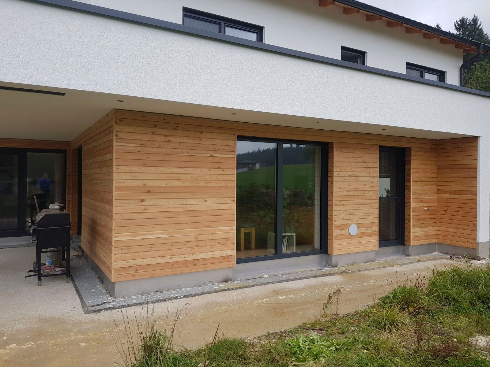 Außenansicht eines modernen Hauses mit Holzverkleidung und großen Fenstern, umgeben von Rasen