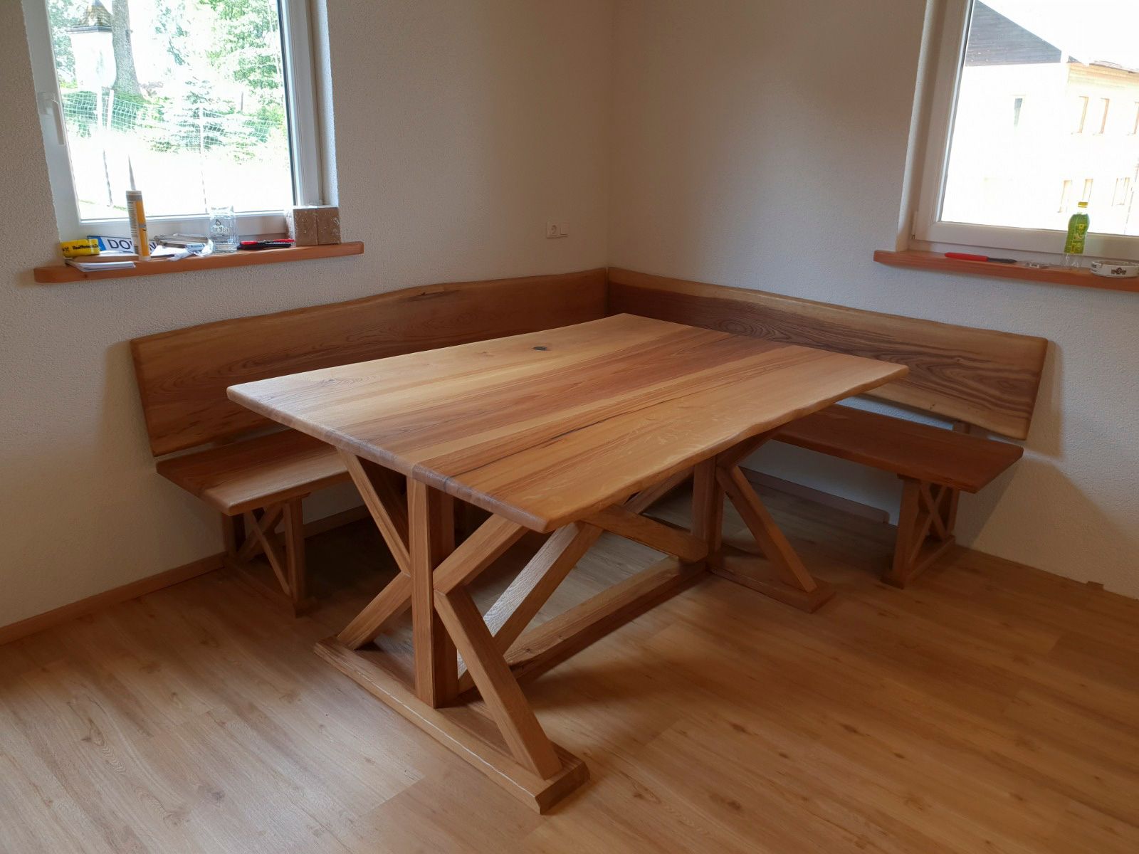 Holzesstisch mit angebauten Eckbänken in einem Zimmer mit zwei Fenstern.