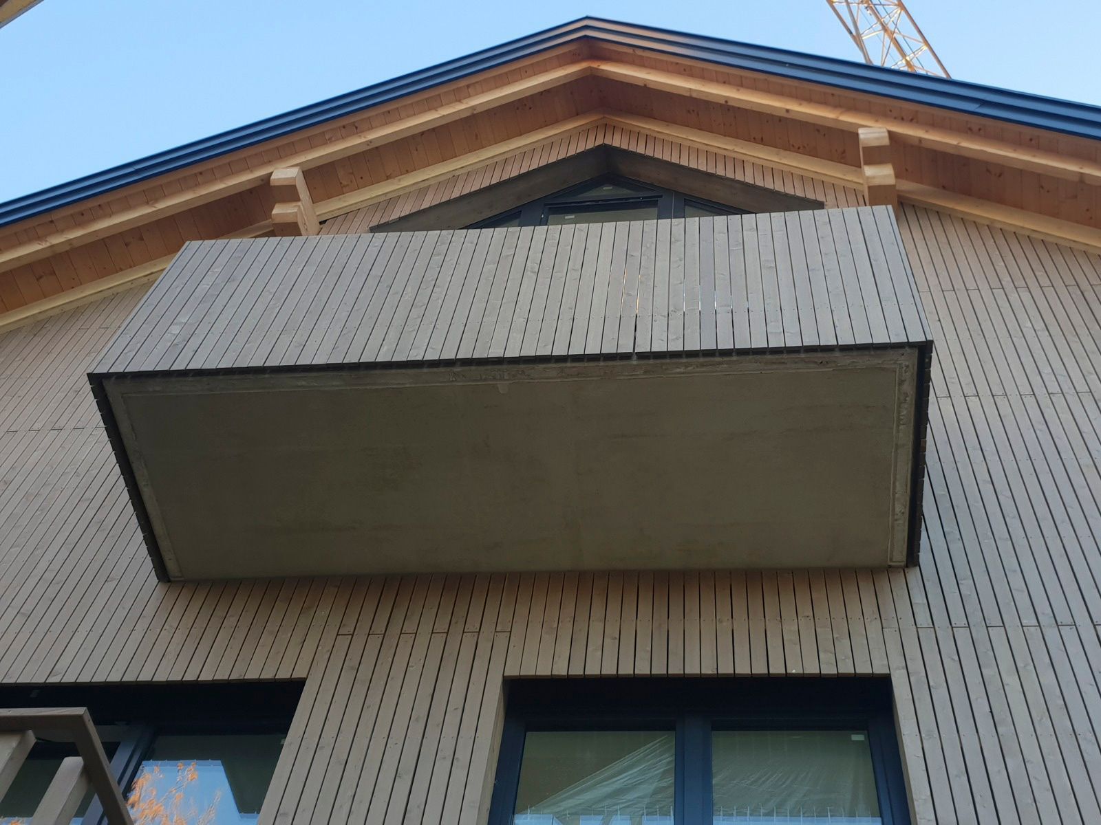 Balkon an einem hellen, holzverkleideten Gebäude mit dunklen Zierelementen.