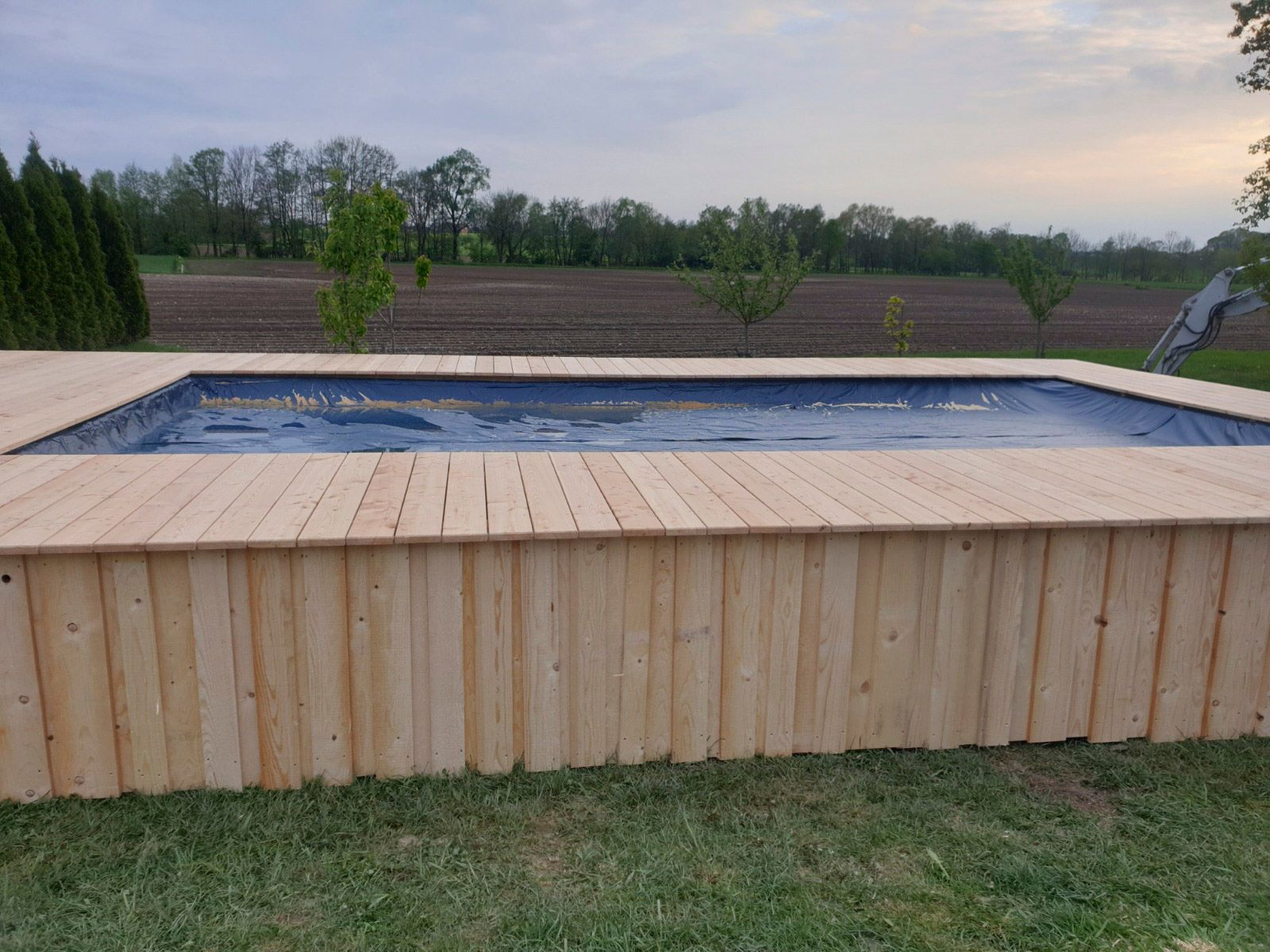 Ein erhöhter, holzumrandeter Pool mit blauer Abdeckung, umgeben von Holzterrasse