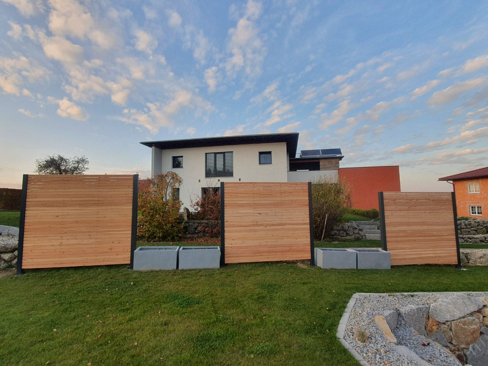 Sichtschutzzaunelemente aus Holz mit Pflanzkästen vor einem Haus in einem Rasengarten.