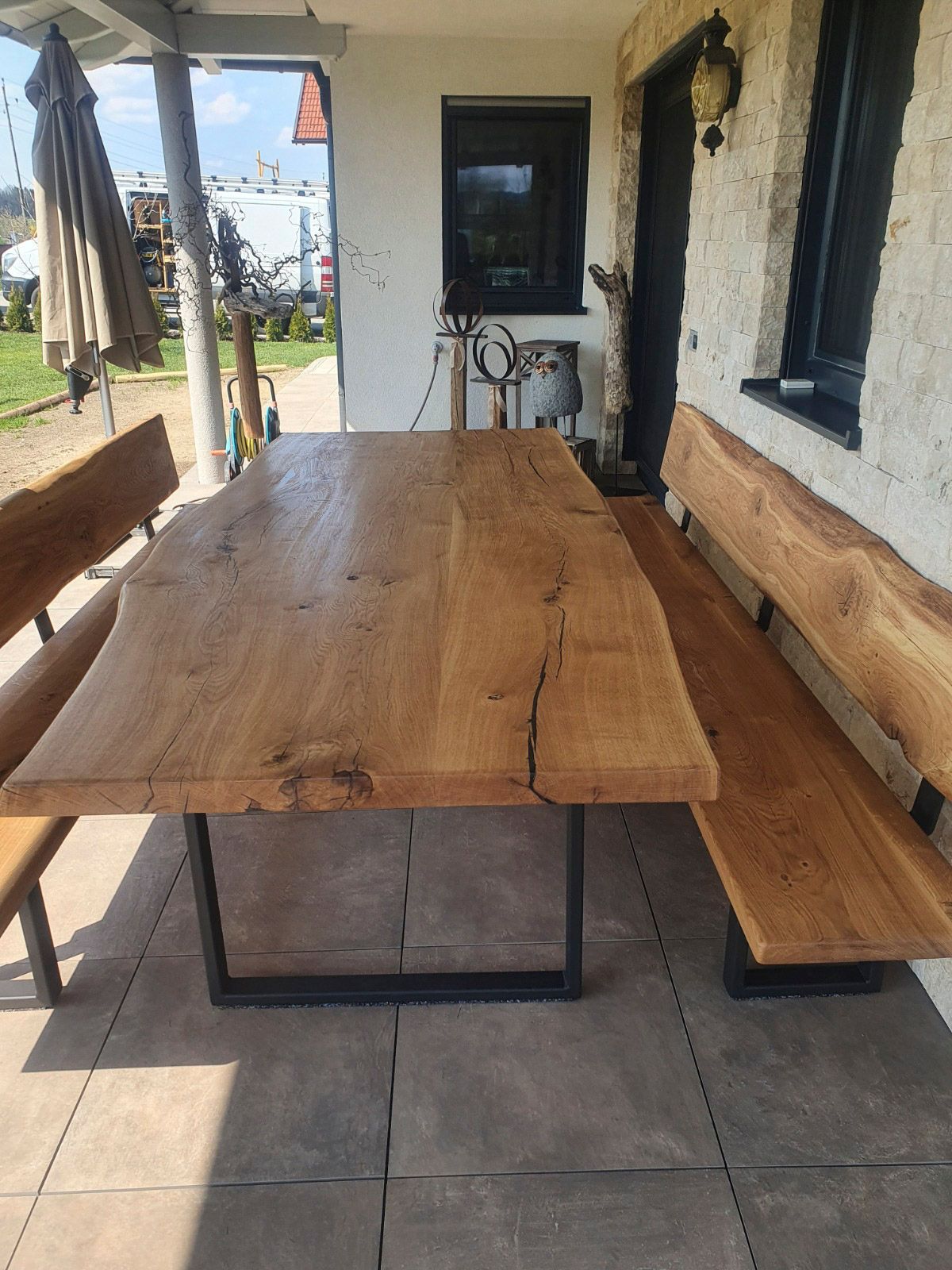 Holzesstisch mit Bänken für den Außenbereich, aufgestellt auf einer überdachten Terrasse.