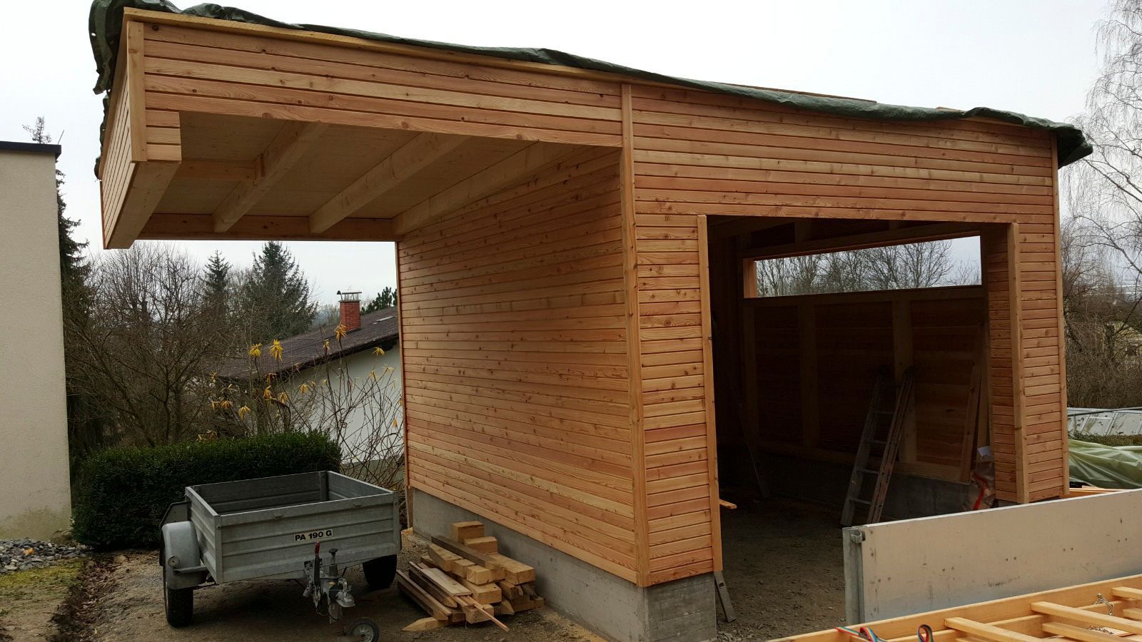 Im Bau befindliche Holzgarage mit angebautem Carport. Hellbraune Holzverkleidung und sichtbare Dachsparren