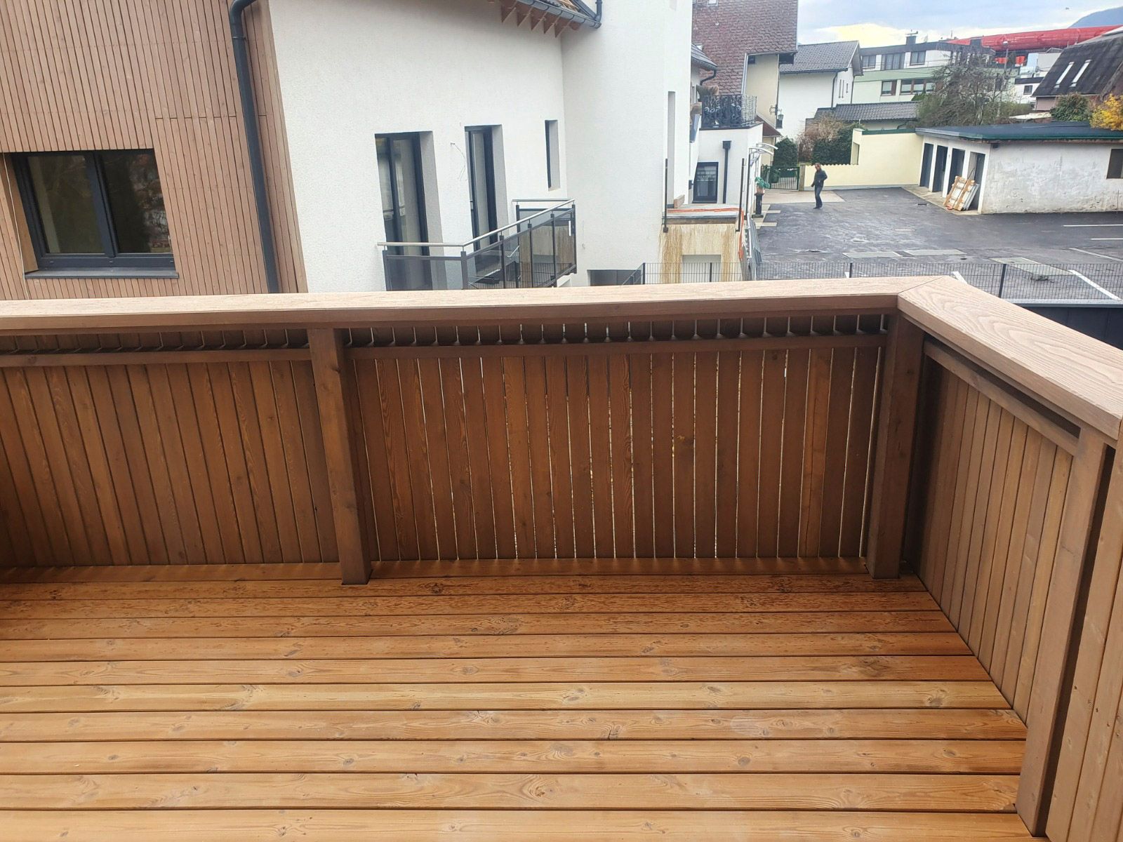 Holzbalkon mit Lattenwänden und Geländer, mit Blick auf eine Straße und Gebäude.