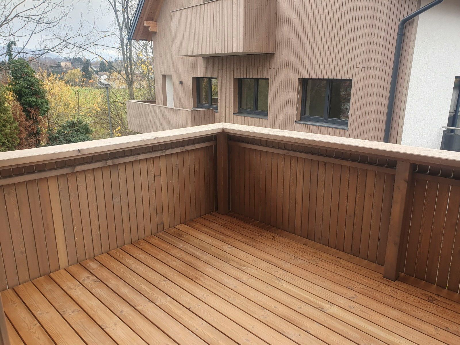 Holzterrasse mit passendem Holzgeländer. Im Hintergrund die Gebäudefassade.