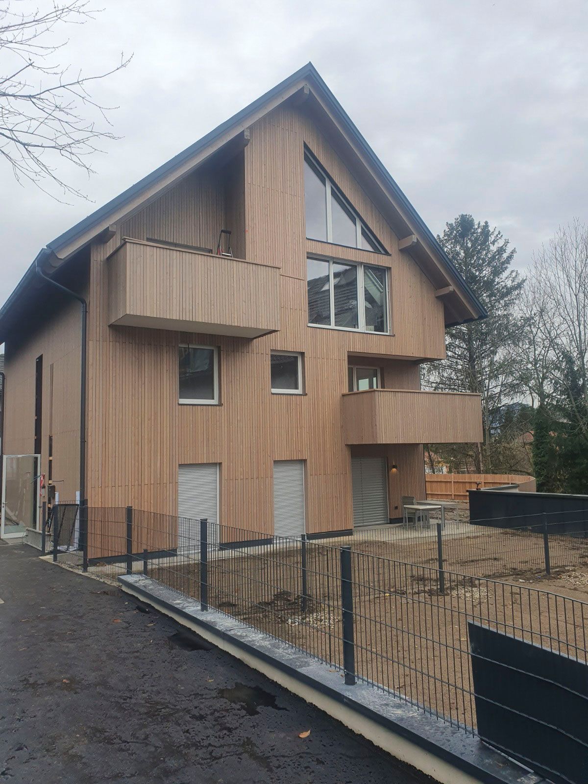 Mehrstöckiges Holzhaus mit zwei Balkonen vor bewölktem Himmel.