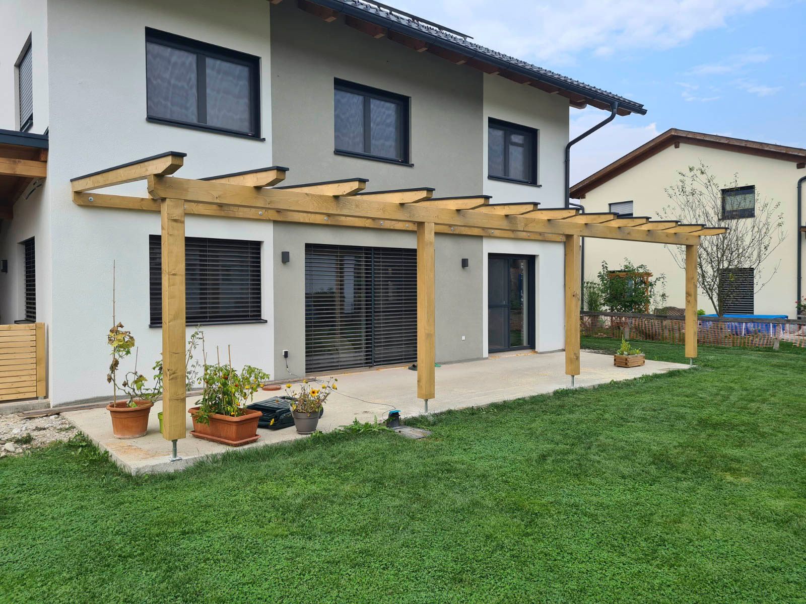 Eine Pergola im Garten eines zweistöckigen Hauses mit Rasenfläche.