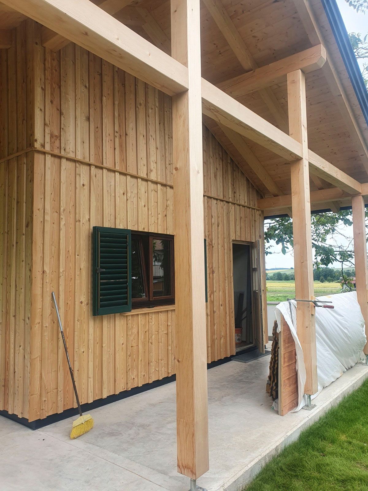 Holzgebäude mit Veranda, Fensterläden und Tür, umgeben von Gras.