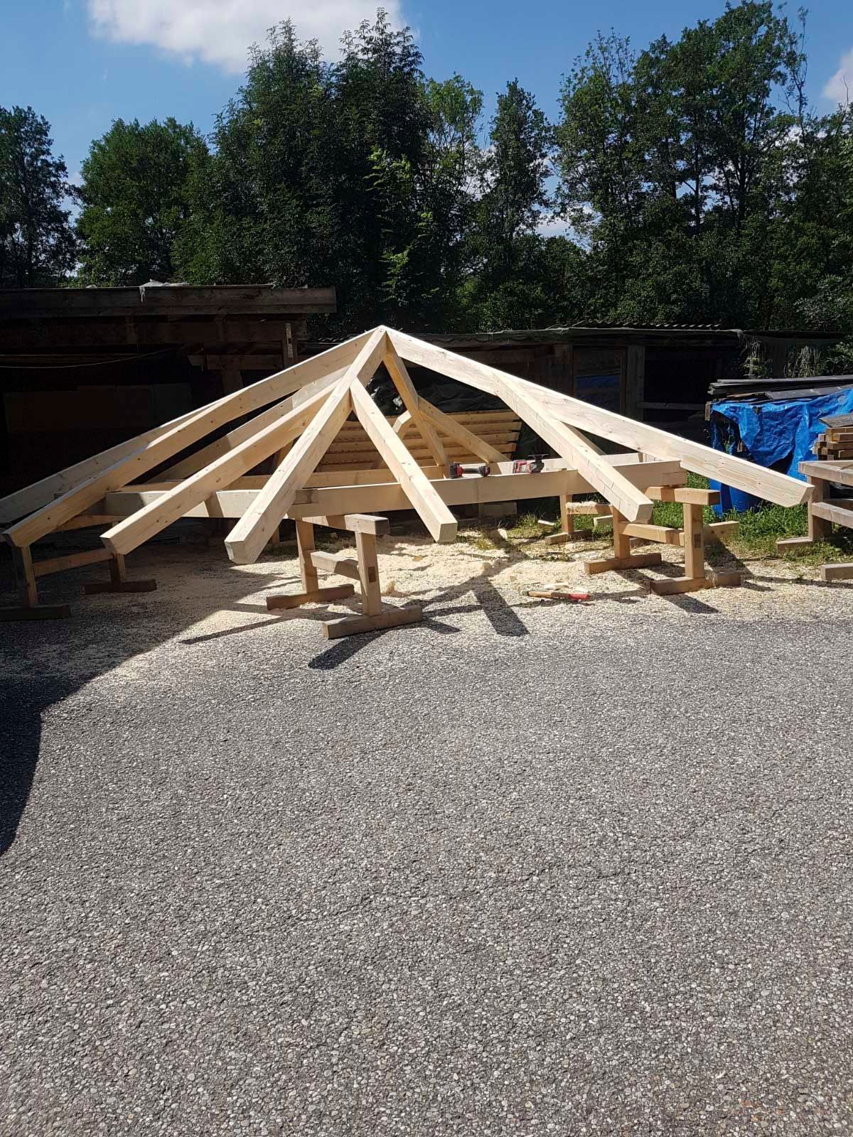 Holzgerüst für einen Pavillon im Bau auf Kiesfläche, im Hintergrund Bäume.