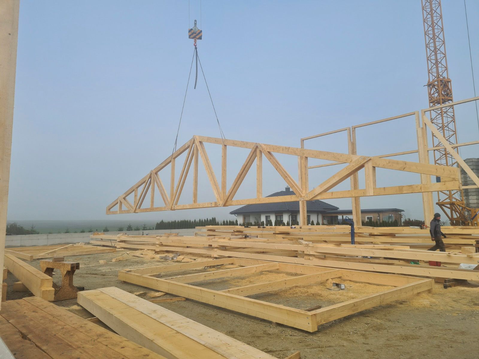 Ein Kran hebt einen großen hölzernen Dachstuhl auf einer Baustelle an.