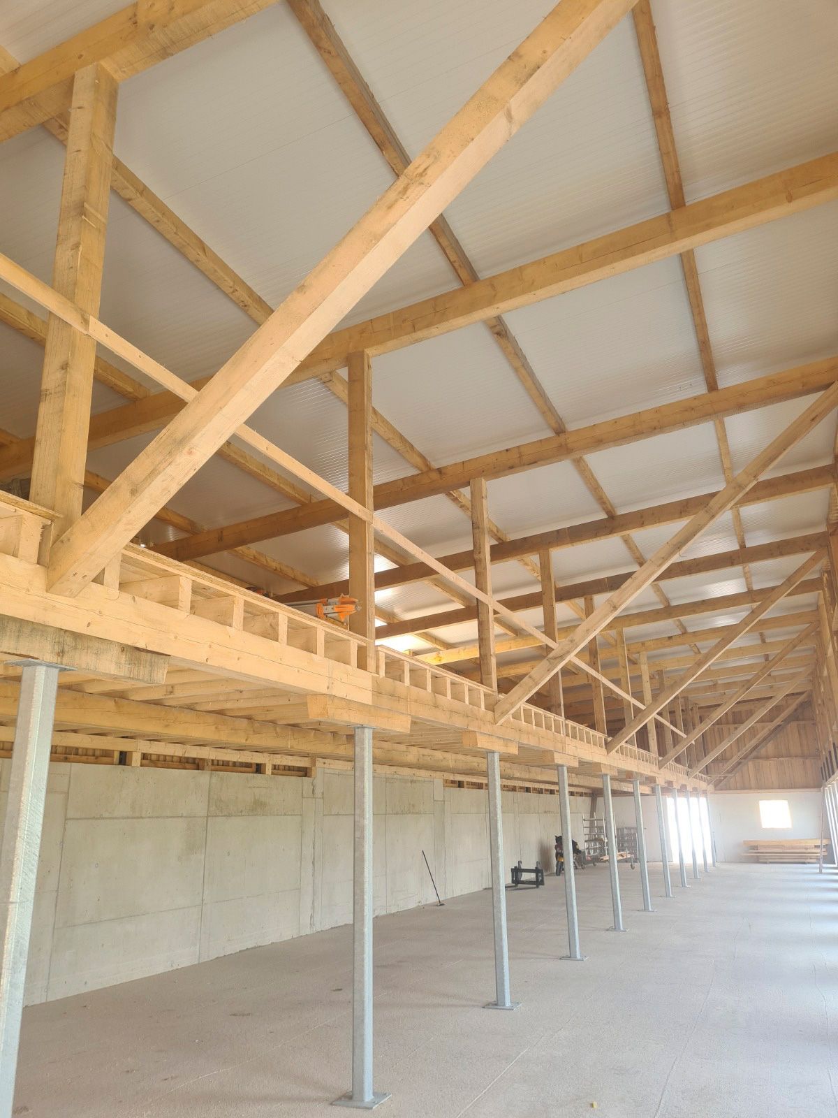 Innenansicht einer im Bau befindlichen Holzscheune mit Balken, Dachsparren und Betonfundament.