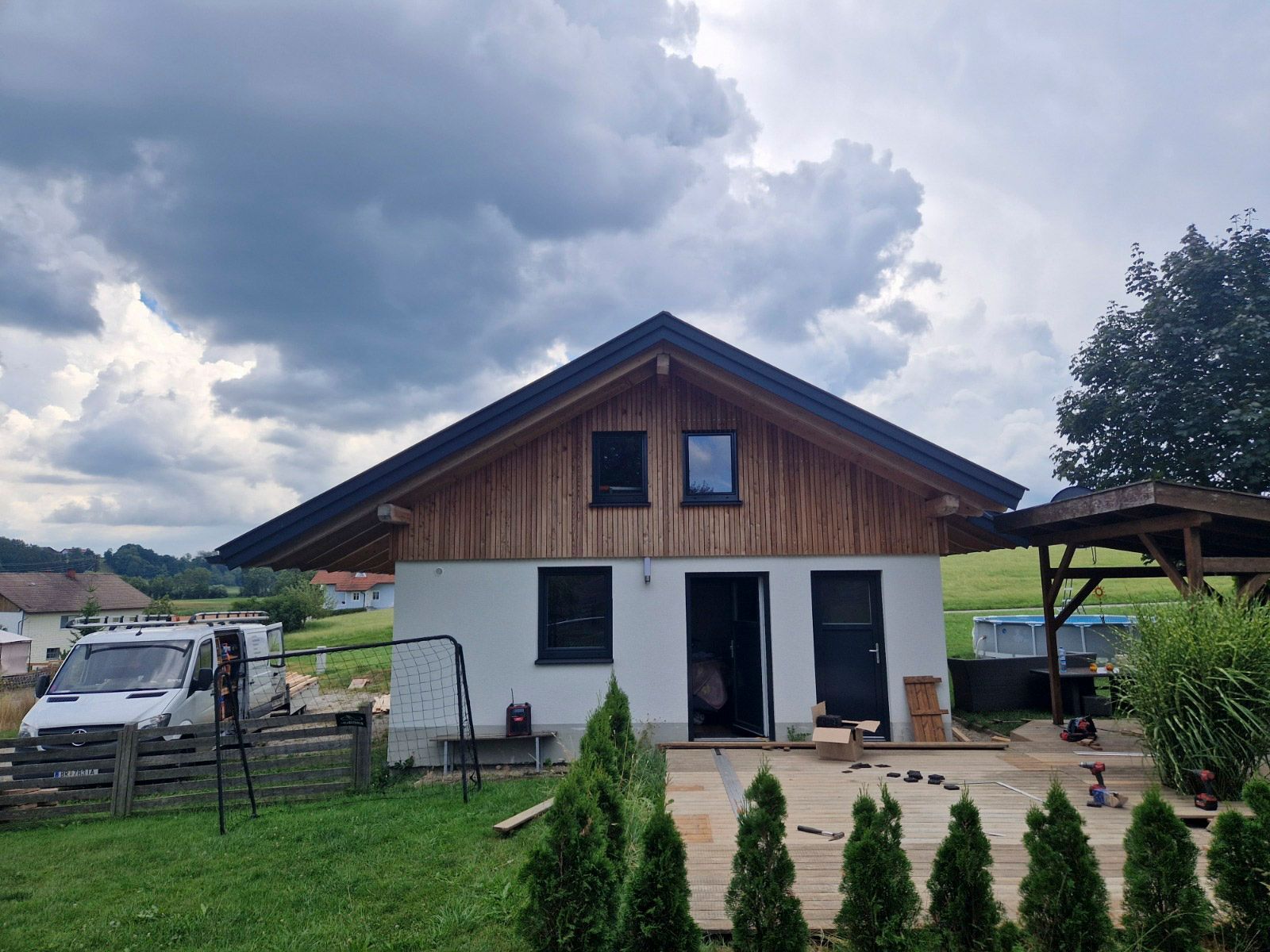 Weißes Haus mit hölzernem Obergeschoss und dunklem Dach; bewölkter Himmel.