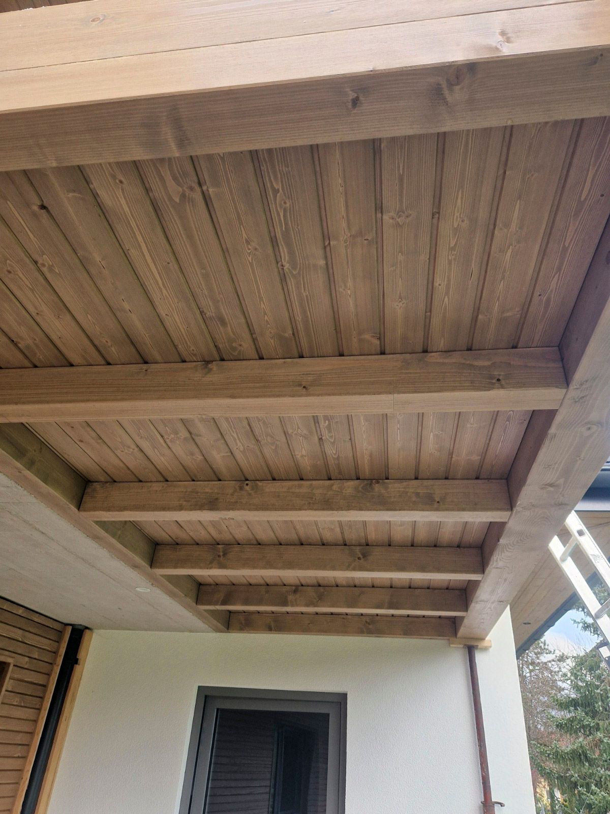 Holzdecke mit Stützbalken, die an der Außenwand eines Gebäudes befestigt ist.