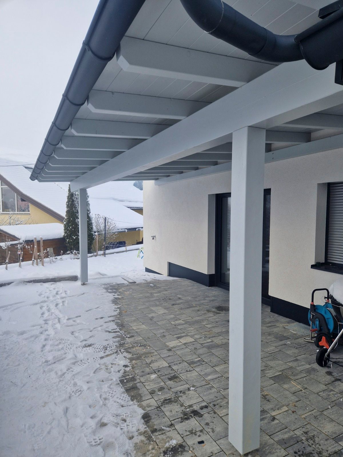 Überdachte Terrasse mit Schnee auf dem Boden; weiße Säulen und Zierleisten, graue Dachrinne.