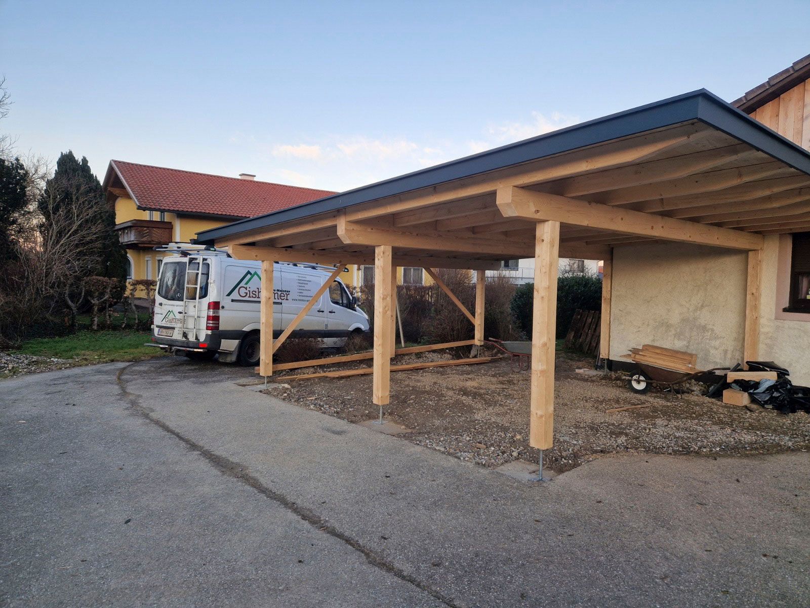 Ein Carport aus Holz neben einem Haus, darunter ein Lieferwagen geparkt.