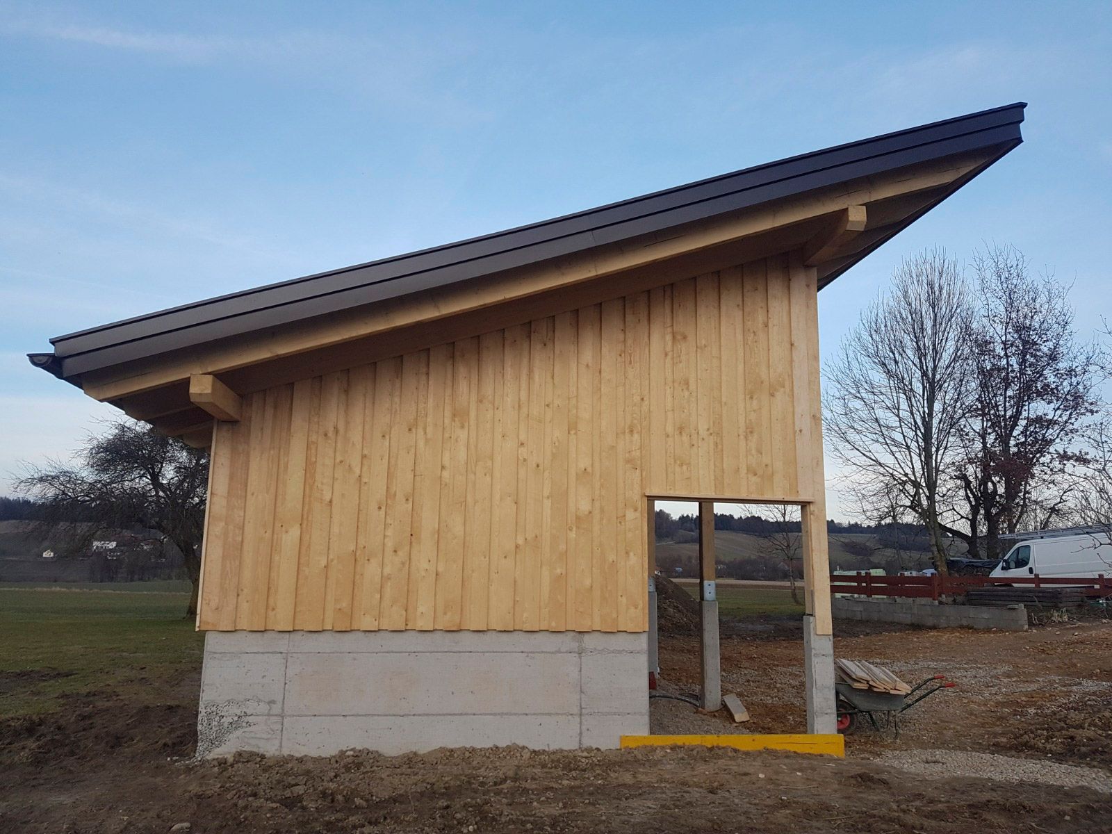 Im Bau befindlicher Holzschuppen mit schrägem, schwarzem Dach und offener Tür auf Betonfundament.
