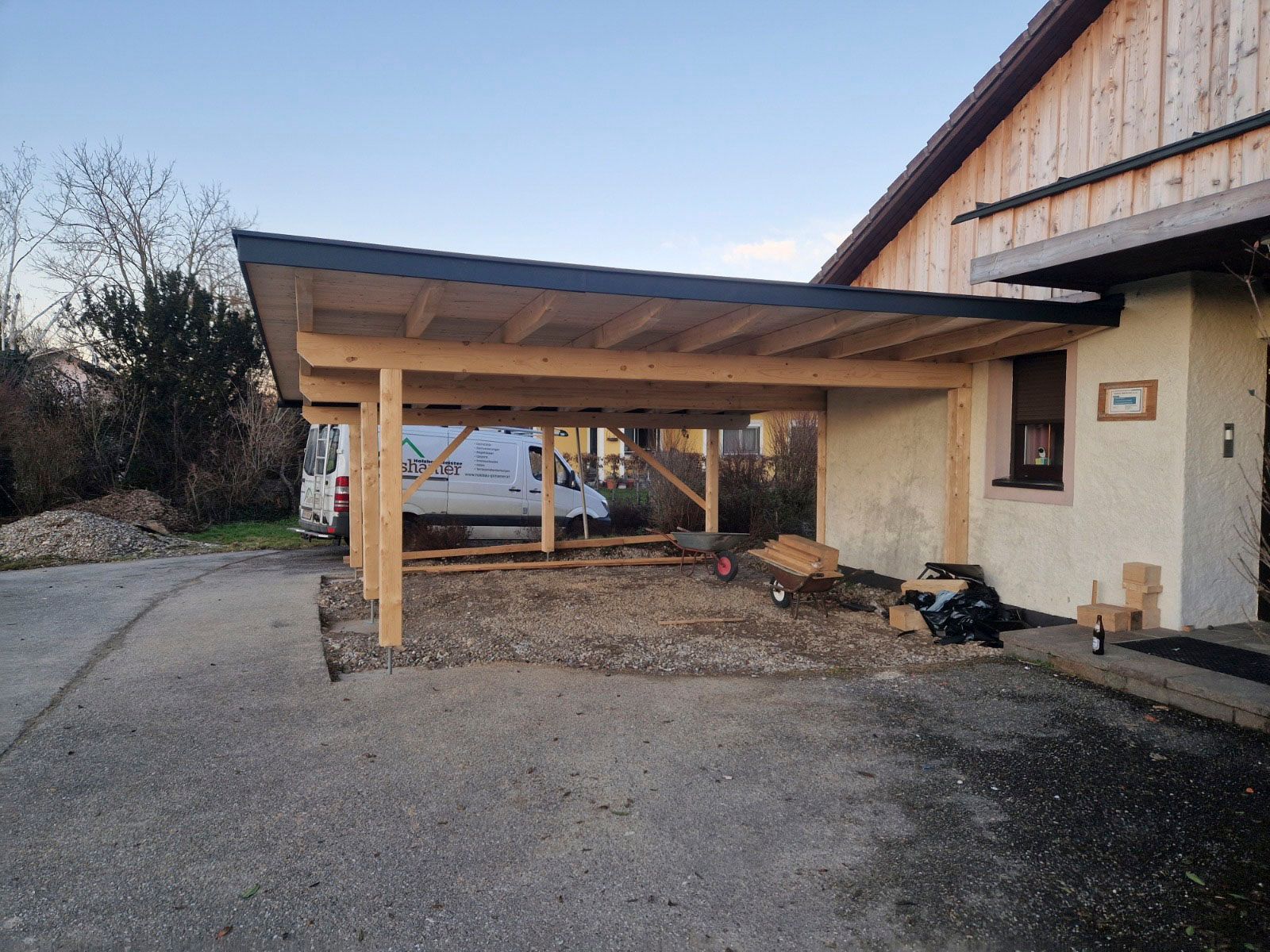 Holzcarport an einem beigen Haus, Kiesauffahrt.