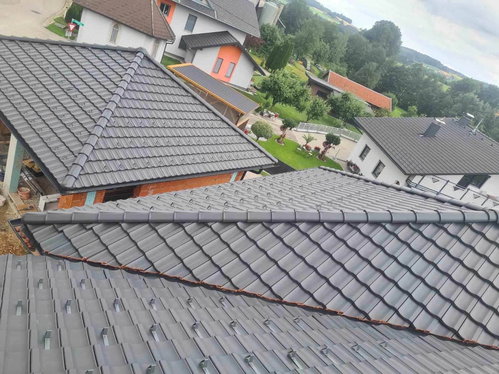 Graue Ziegeldächer mehrerer Häuser vor einer grünen Landschaft.