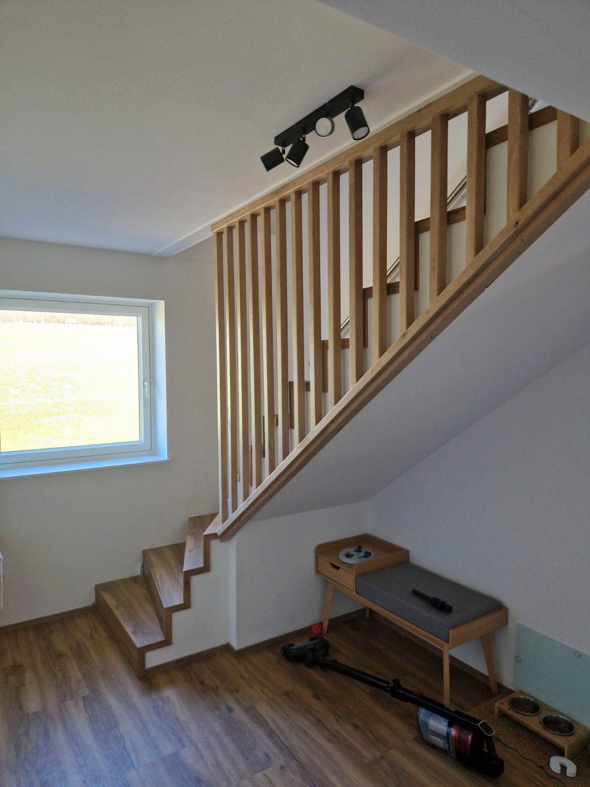 Holztreppe mit Geländer und Einbauleuchten. Am Fuß der Treppe befinden sich eine kleine Bank und ein Staubsauger.