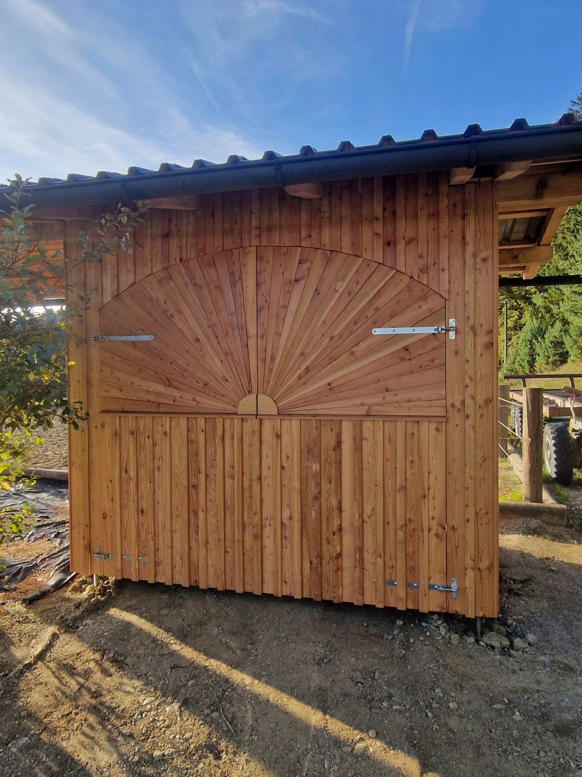 Ein Holzschuppen mit einem sonnenförmigen Muster auf den Türen unter blauem Himmel.