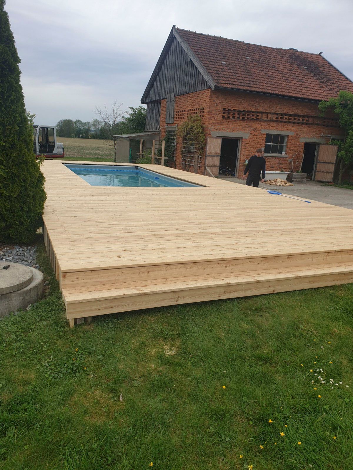 Pool mit Holzterrasse vor einem Backsteingebäude.