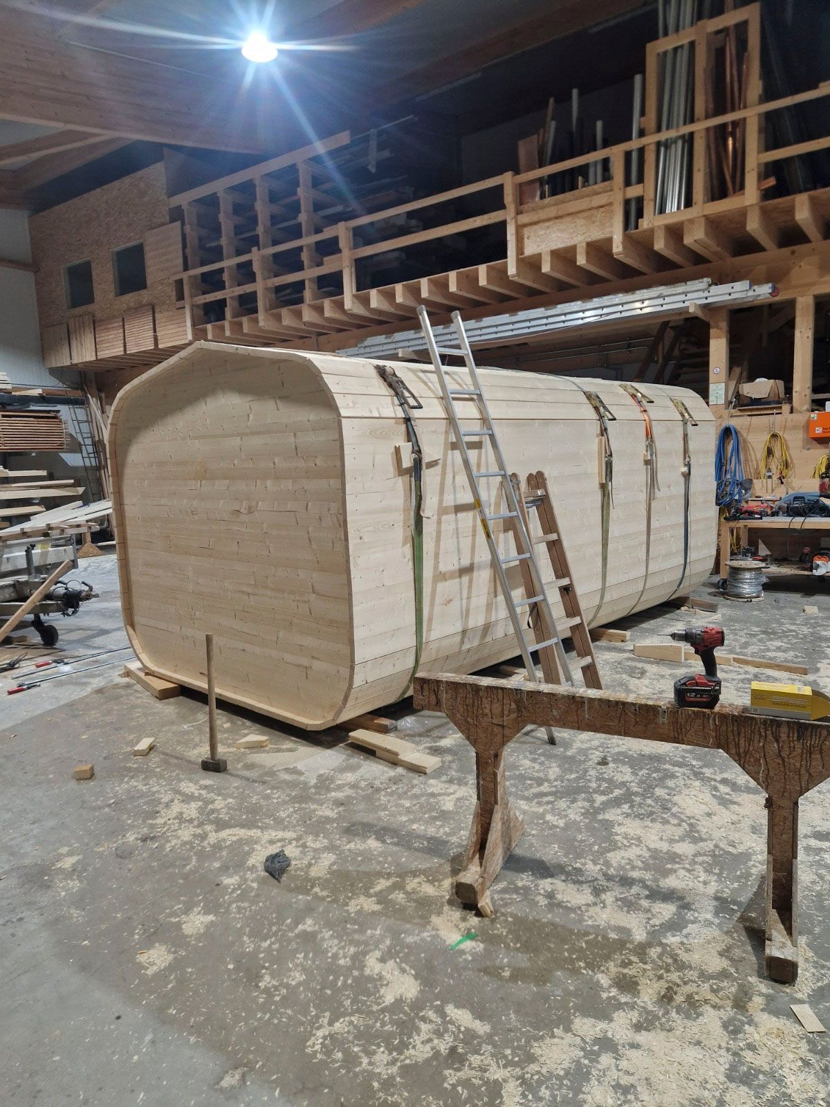 Eine große Holzkonstruktion befindet sich in einer Werkstatt im Bau; sie ist mit Gurten gesichert