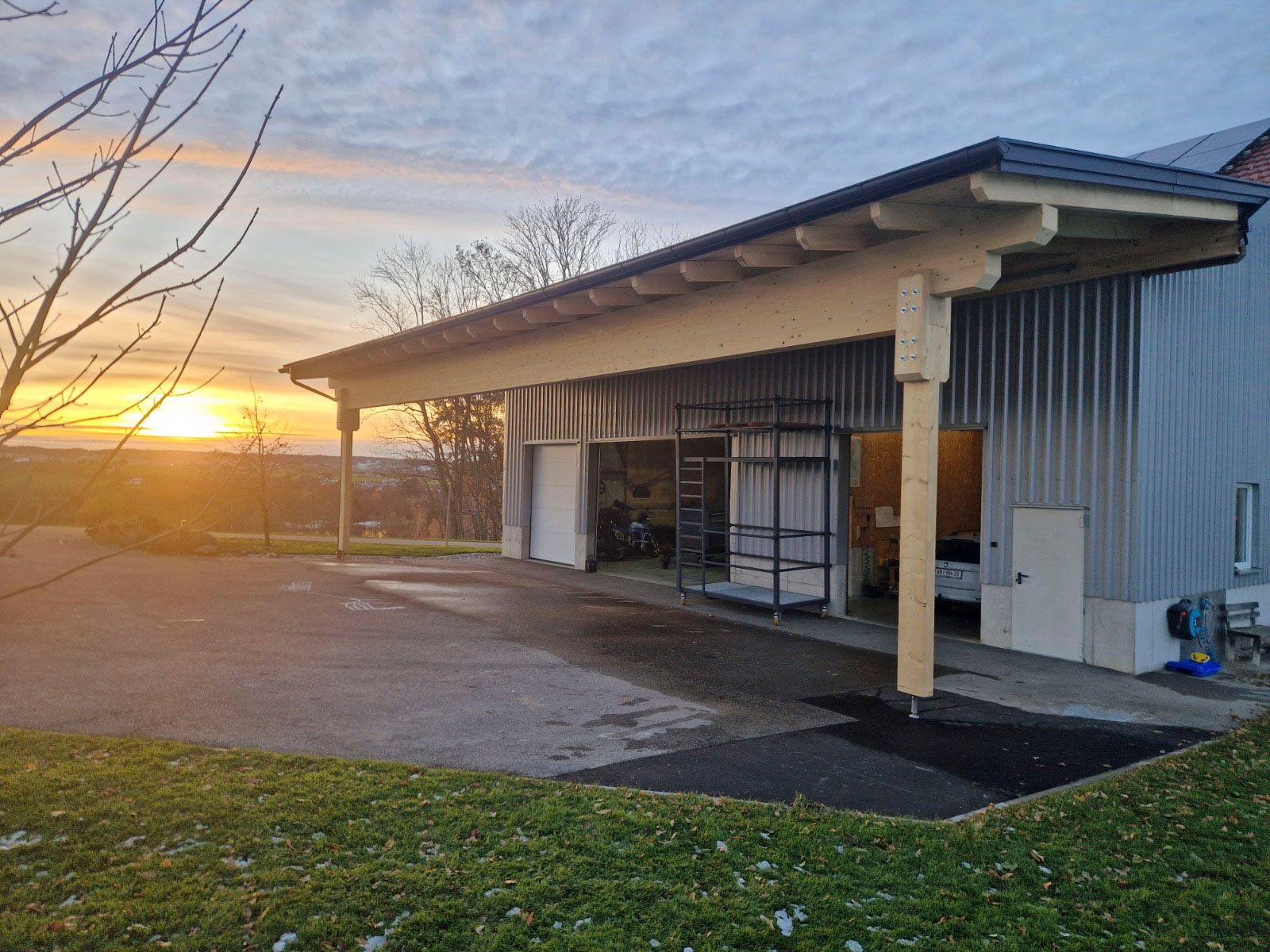 Holzcarport mit Metallgebäude, Sonnenaufgang im Hintergrund.