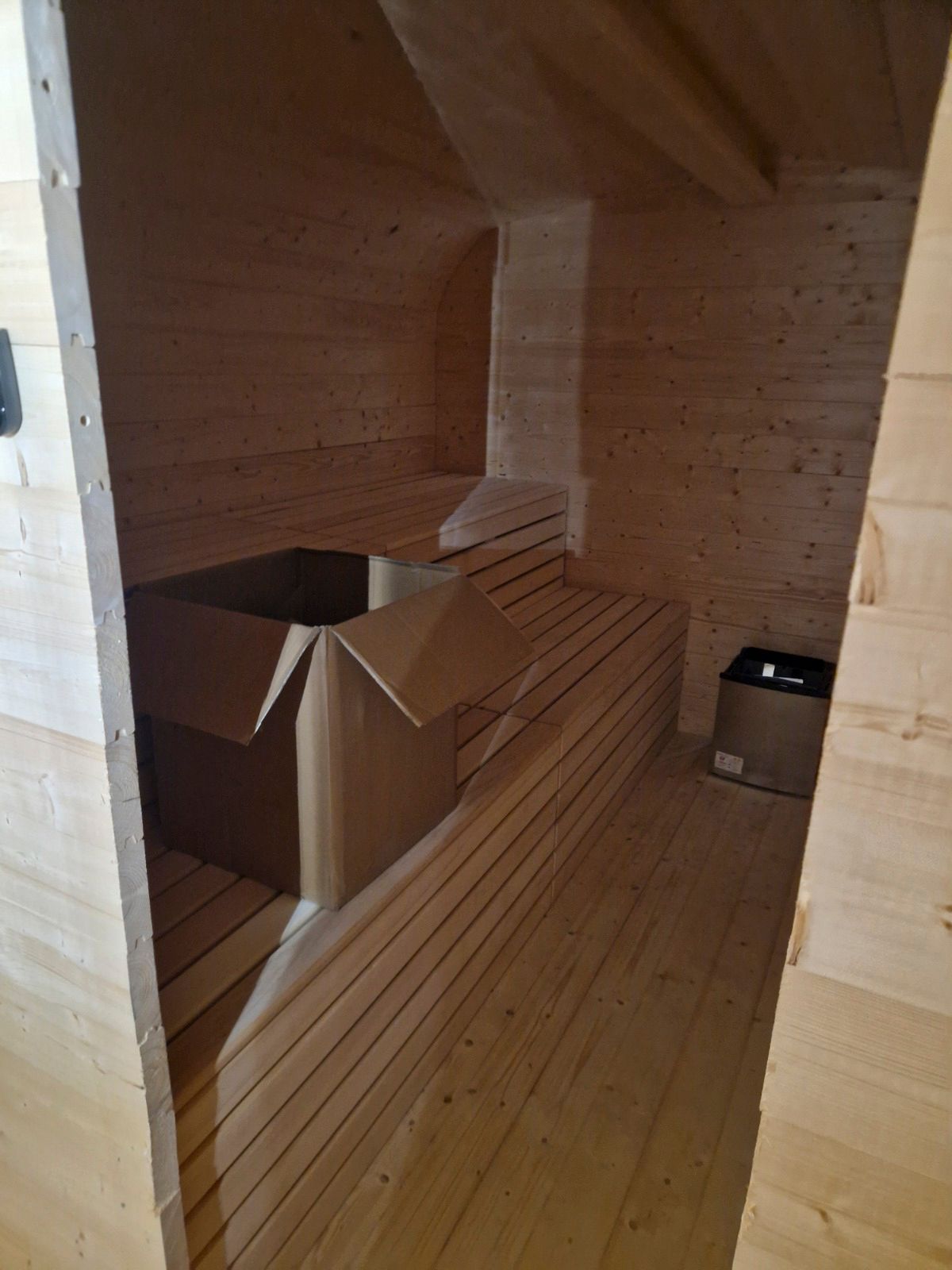 Saunainterieur aus Holz mit Bänken, Pappkartons und einer schrägen Decke.