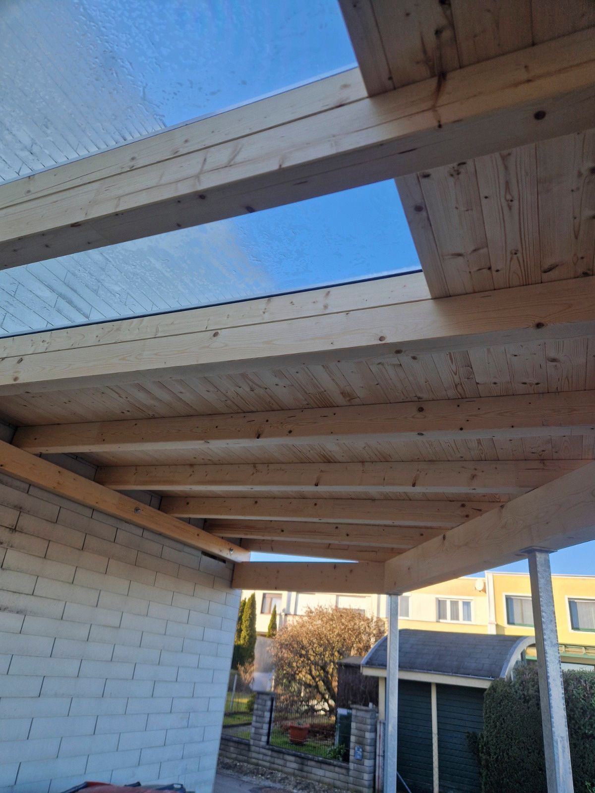 Pergola-Dach aus Holz mit transparenten Paneelen, Blick auf den blauen Himmel.