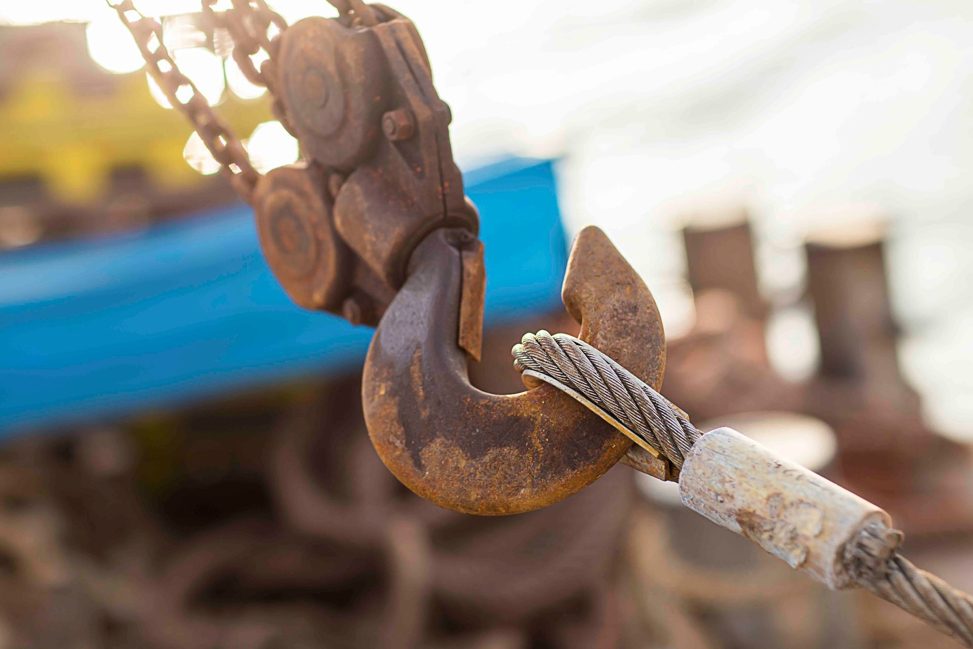 Rostiger Metallhaken, der ein Stahlseil hält, mit Kette und blauem Hintergrund.