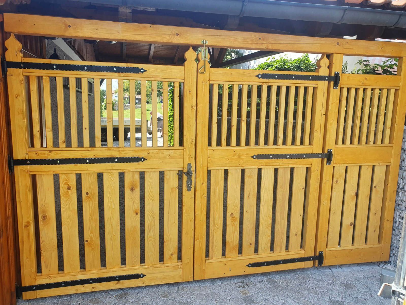 Holztor mit vertikalen Latten, hellbraune Farbe, schwarze Beschläge, gewölbter Abschluss, für den Außenbereich.