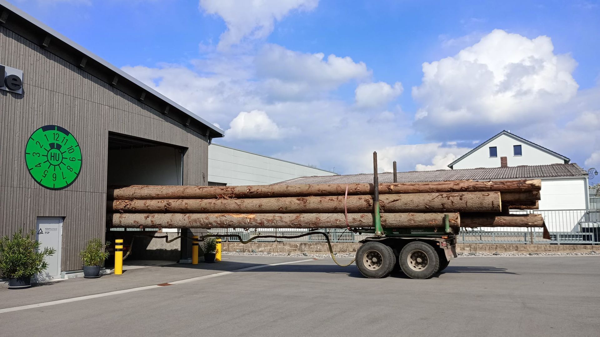 Ein Holztransporter transportiert lange Baumstämme neben einem Lagerhaus an einem sonnigen Tag