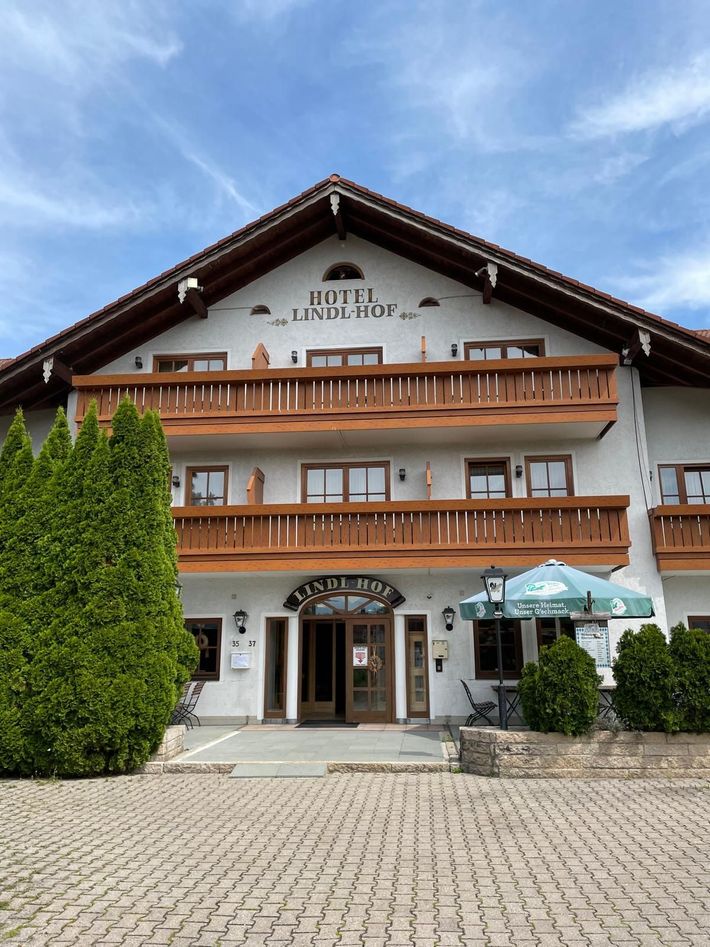 Hotel mit Holzbalkonen und einem grünen Sonnenschirm. Weiße Wände, braune Zierleisten und ein gepflasterter Bereich.