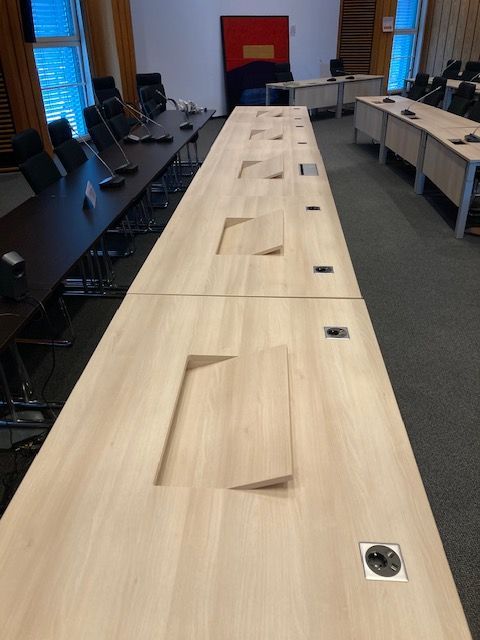 Lange Konferenztische mit Steckdosen und Stühlen in einem gut beleuchteten Raum.