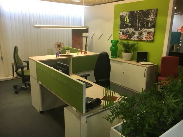 Modernes Büro mit grünen Akzenten, Schreibtisch, Stuhl, Kunstwerken und Pflanzen.