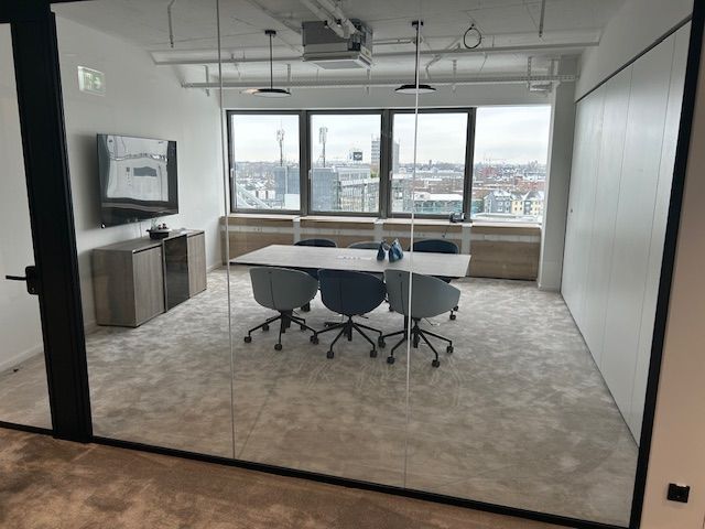 Konferenzraum mit Glaswänden, Tisch, Stühlen, Fenstern und Blick auf die Stadt.