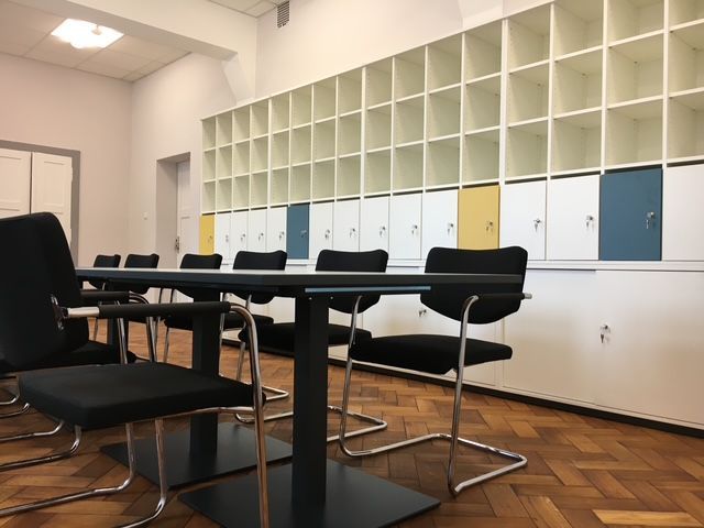 Besprechungsraum mit schwarzem Tisch, Stühlen und an der Wand montierten Fächern mit weißen und farbigen Paneelen.