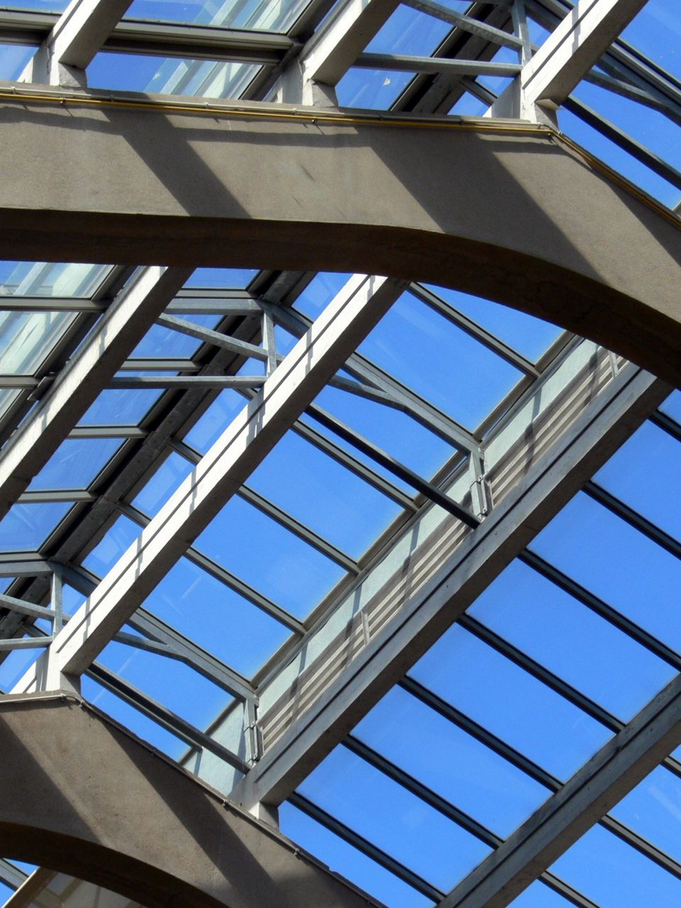 Puits de lumière avec ciel bleu visible à travers des vitres et des poutres de support grises.