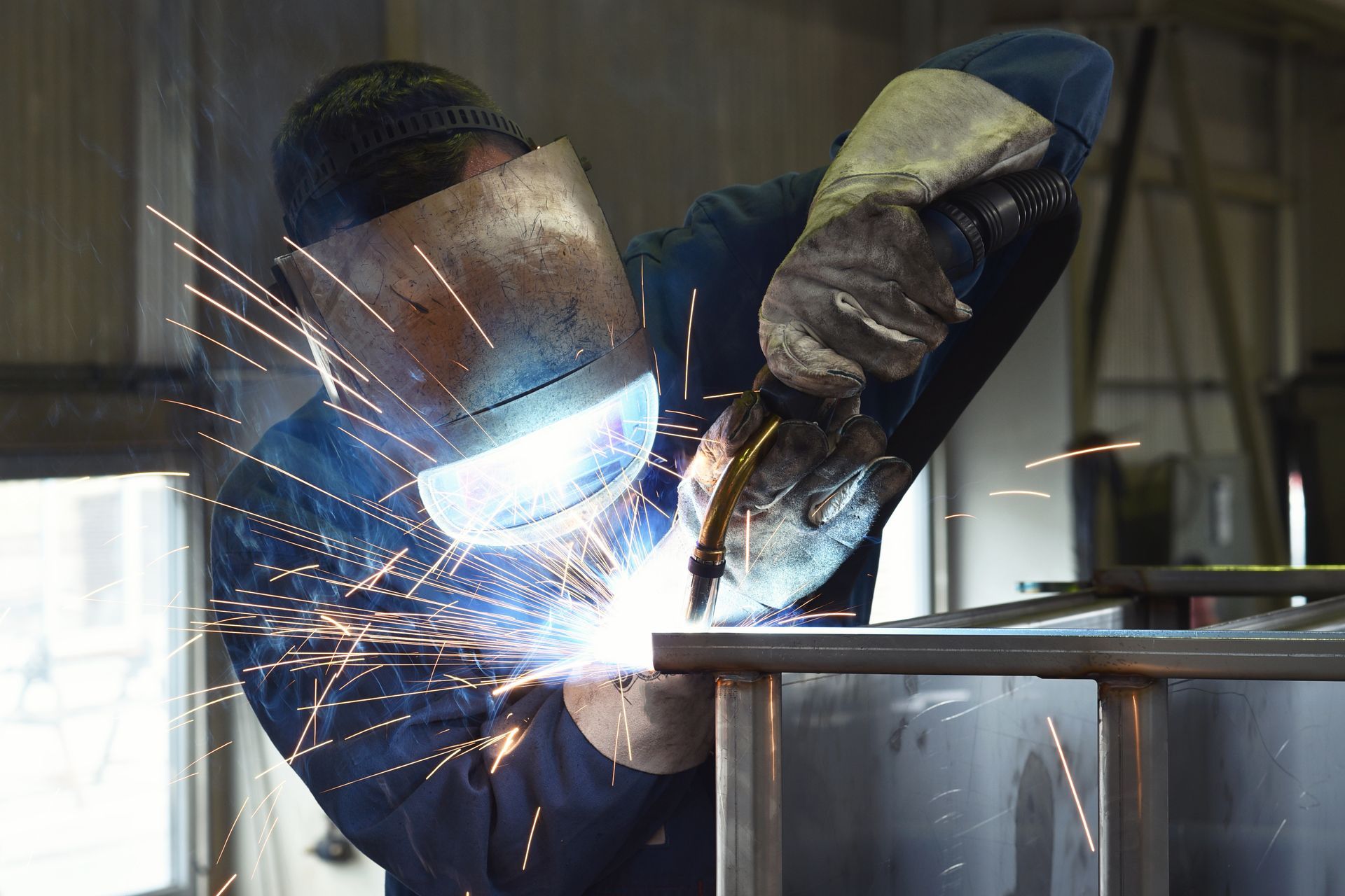 Soudeur en équipement de protection utilisant un chalumeau sur une structure métallique, créant des étincelles.