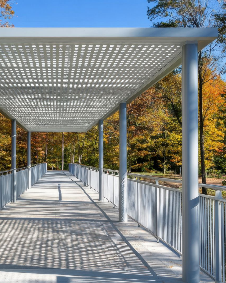 Passerelle couverte avec un toit à motifs, une balustrade et des colonnes grises, dans un parc au feuillage d'automne coloré.