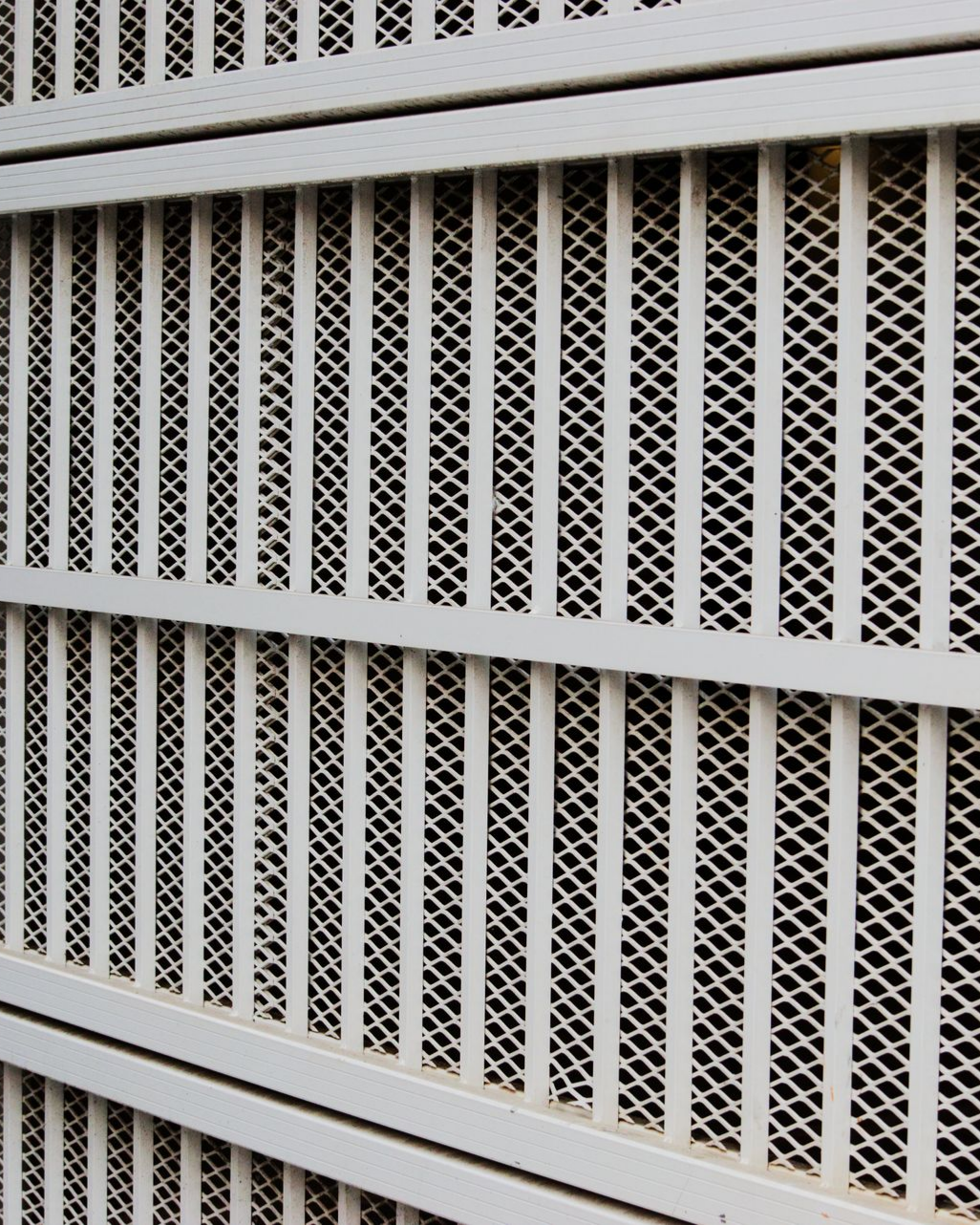 Grille de sécurité en métal blanc avec barreaux verticaux et maille en forme de losange.